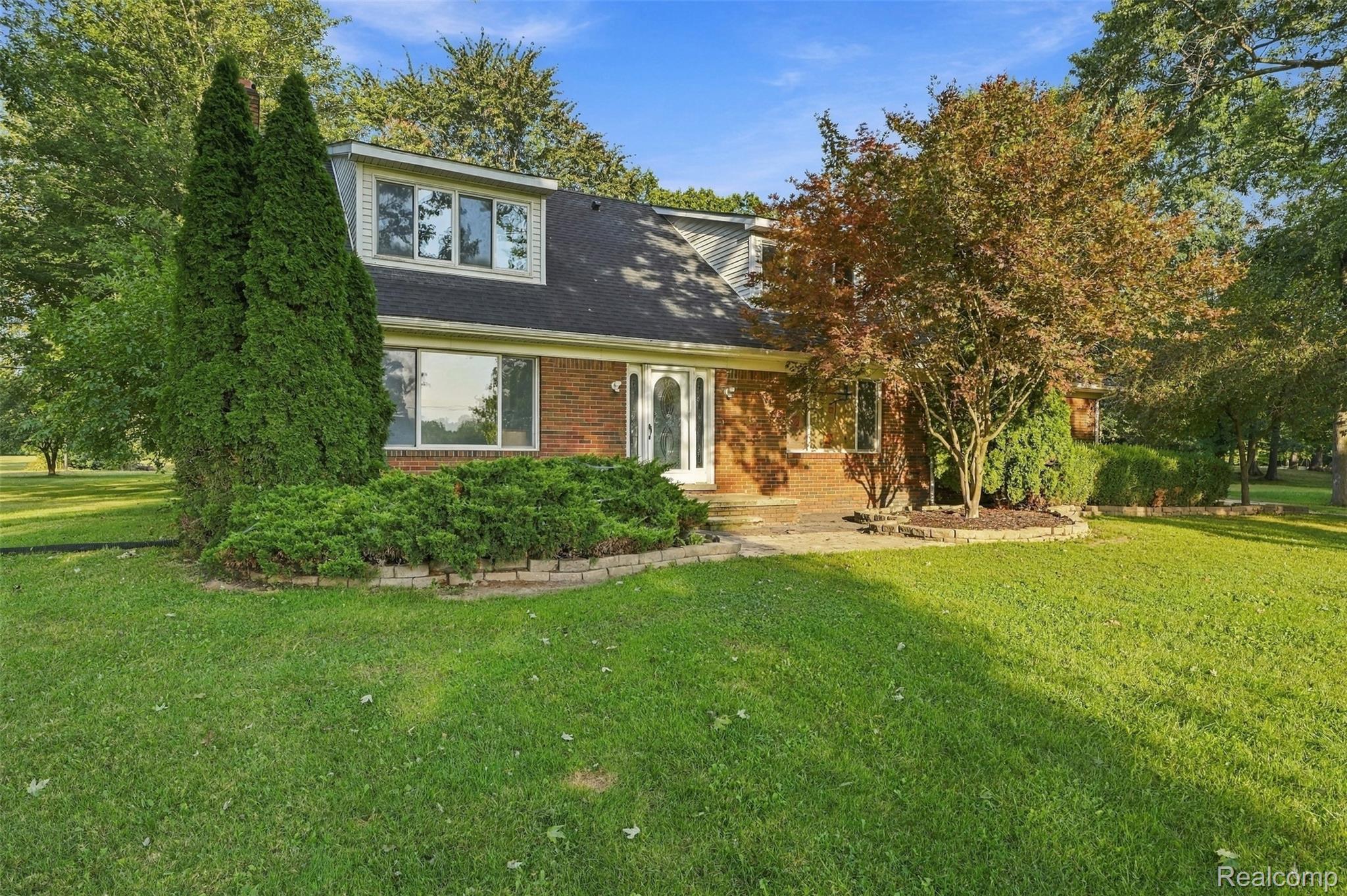Brick exterior with dormer windows, dark shingle roof, and established landscaping
