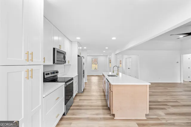 a large kitchen with stainless steel appliances kitchen island a stove a refrigerator a oven and white cabinets with wooden floor