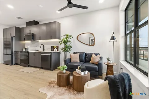 a living room with stainless steel appliances kitchen island granite countertop a stove a sink dishwasher and a view of kitchen appliances with wooden floor