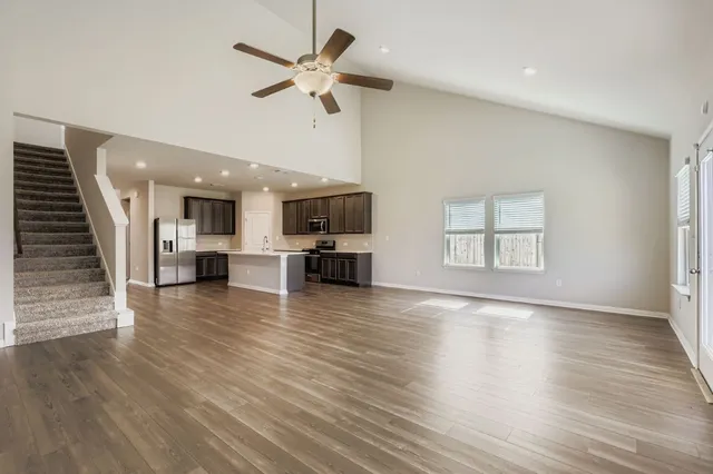 an empty room with wooden floor a ceiling fan and windows