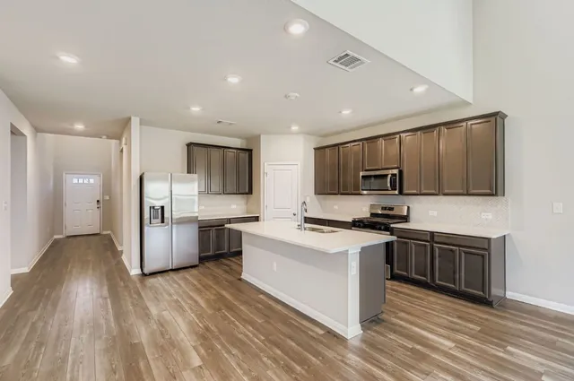 a kitchen with stainless steel appliances a stove top oven a sink a refrigerator white cabinets and wooden floor