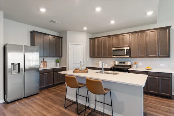 a large kitchen with stainless steel appliances a stove a sink dishwasher and a refrigerator with wooden floor