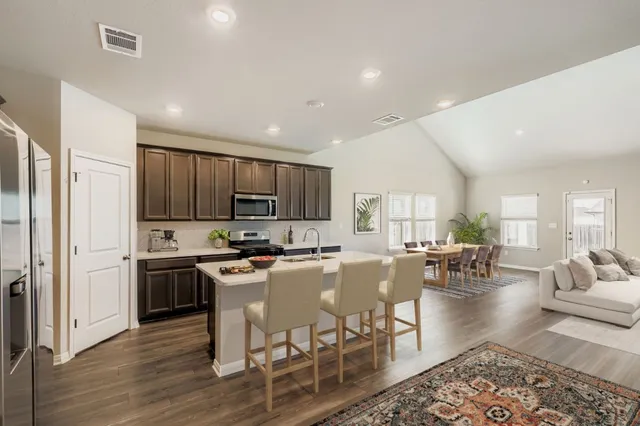 a kitchen with stainless steel appliances granite countertop a stove top oven a refrigerator a sink a dining table and chairs with wooden floor