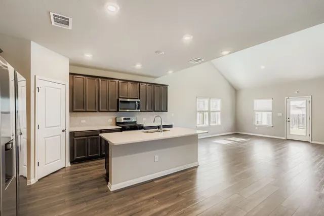 a kitchen with stainless steel appliances a stove top oven a sink a refrigerator cabinets and wooden floor