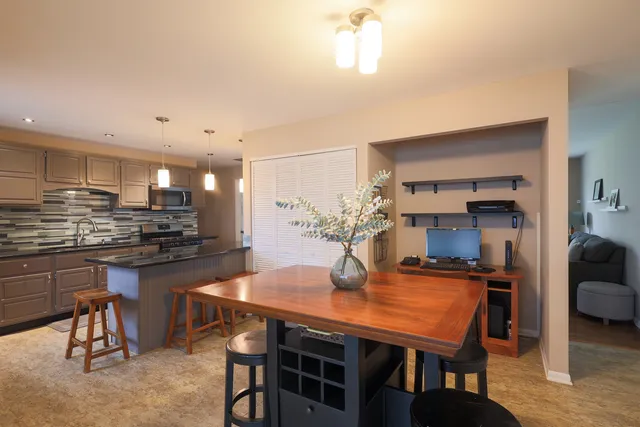 a kitchen with stainless steel appliances kitchen island granite countertop a dining table chairs stove refrigerator and cabinets