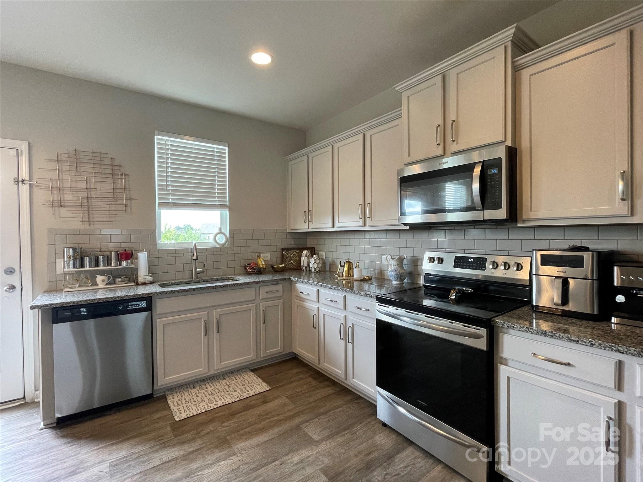 12417 Bryton Ridge Parkway Huntersville, NC 28078 - Photo 5 of 17 a kitchen with stainless steel appliances granite countertop a stove top oven a sink dishwasher and white cabinets with wooden floor