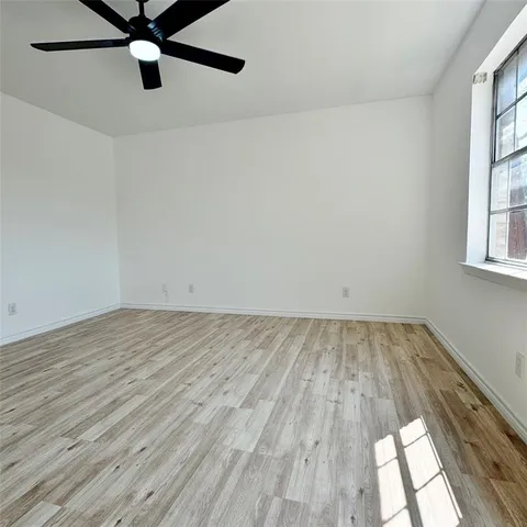 an empty room with wooden floor fan and windows