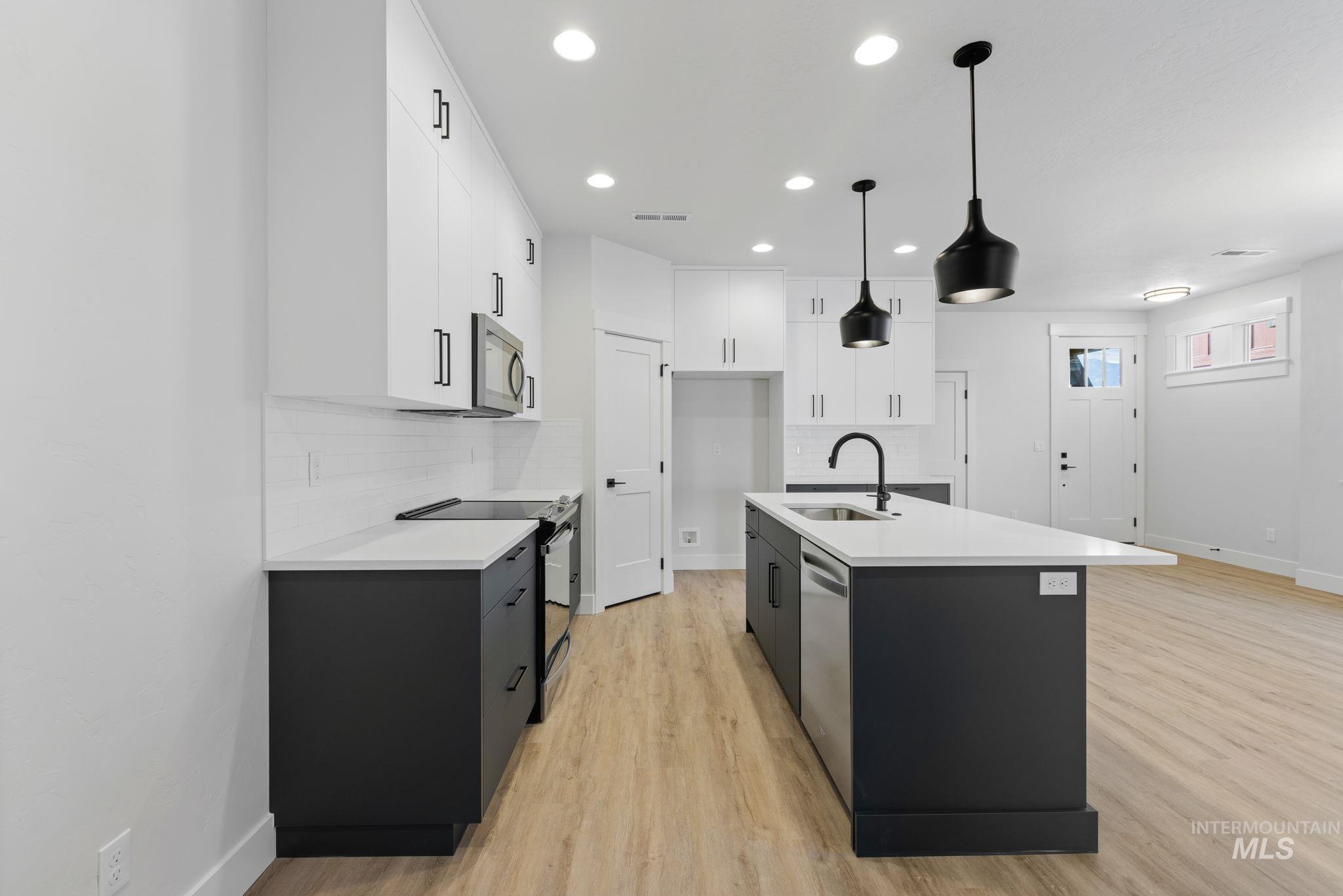22 Bridger Street Cascade, ID 83611 - Photo 12 of 39 Kitchen featuring white cabinetry, appliances with stainless steel finishes, dark cabinets, backsplash, and light wood-style flooring