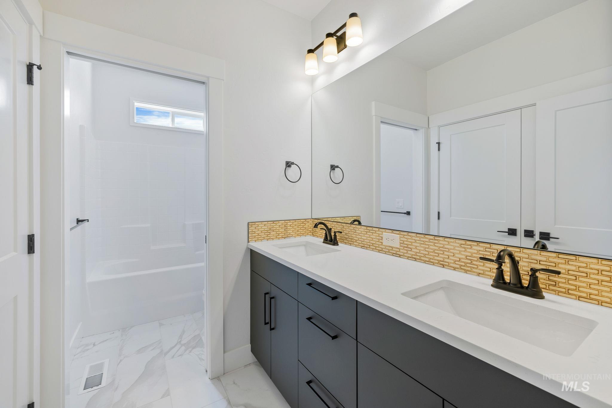 22 Bridger Street Cascade, ID 83611 - Photo 31 of 39 Full bathroom featuring backsplash, double vanity, light marble finish floors, and bathtub / shower combination