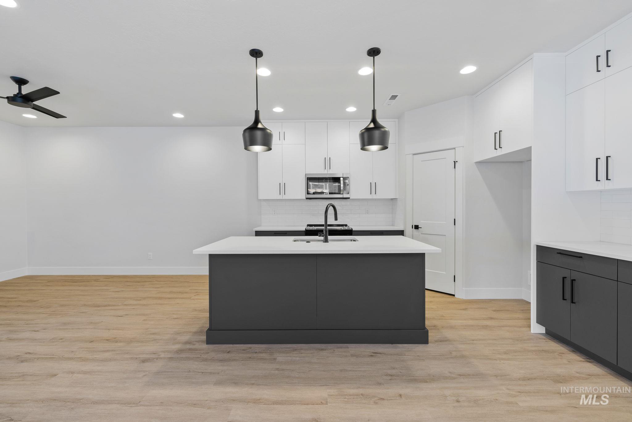 22 Bridger Street Cascade, ID 83611 - Photo 10 of 39 Kitchen featuring decorative backsplash, white cabinetry, light wood-style flooring, a center island with sink, and recessed lighting