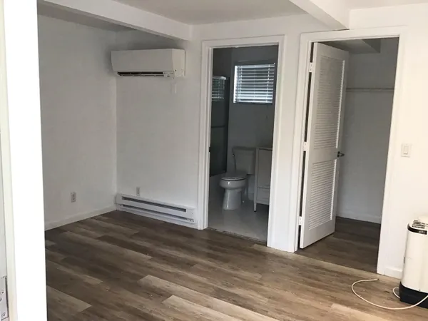 a view of an empty room with wooden floor and a bathroom