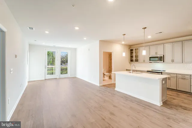 a large white kitchen with kitchen island a sink wooden floor and stainless steel appliances