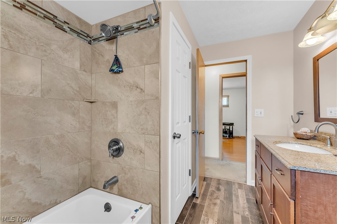 3023 Norris Avenue Cleveland, OH 44134 - Photo 26 of 41 Bathroom featuring wood-finish flooring, a vanity with an integrated sink and stone countertop, and a tiled shower/tub combination with a decorative mosaic accent
