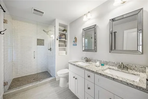 a bathroom with a granite countertop double vanity sink mirror and shower