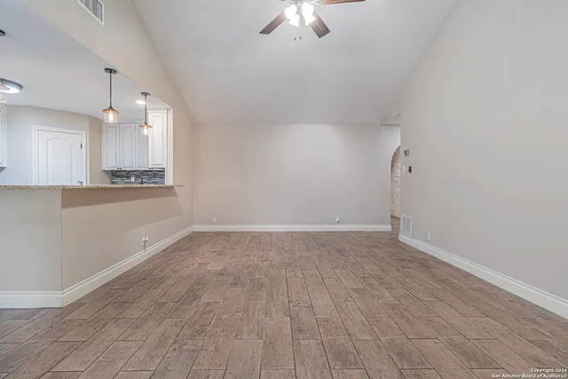 an empty room with wooden floor fan and windows
