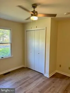 an empty room with wooden floor ceiling fan and window