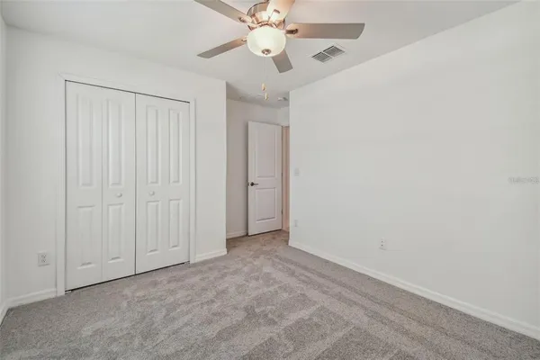 an empty room with a chandelier fan and closet area
