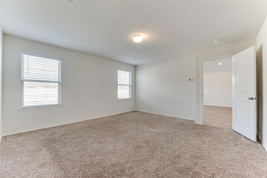 517 Milo Way Royse City, TX 75189 - Photo 8 of 34 Spacious room featuring neutral carpeting, white walls, two windows with blinds, a ceiling-mounted light fixture, and an open doorway revealing wood-finish flooring in the adjacent room