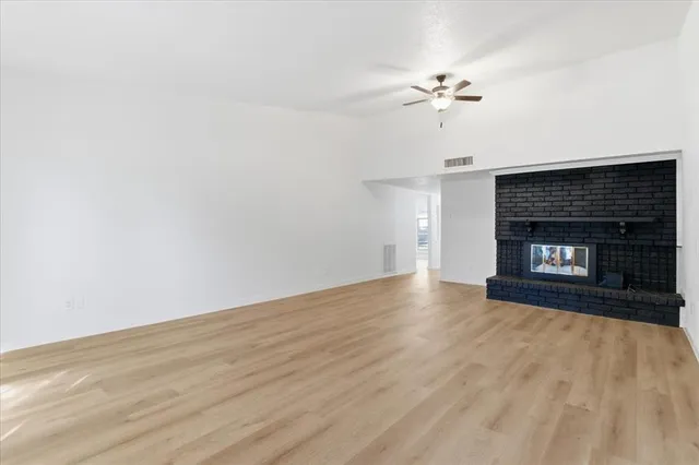 a view of an empty room with wooden floor fireplace and a window