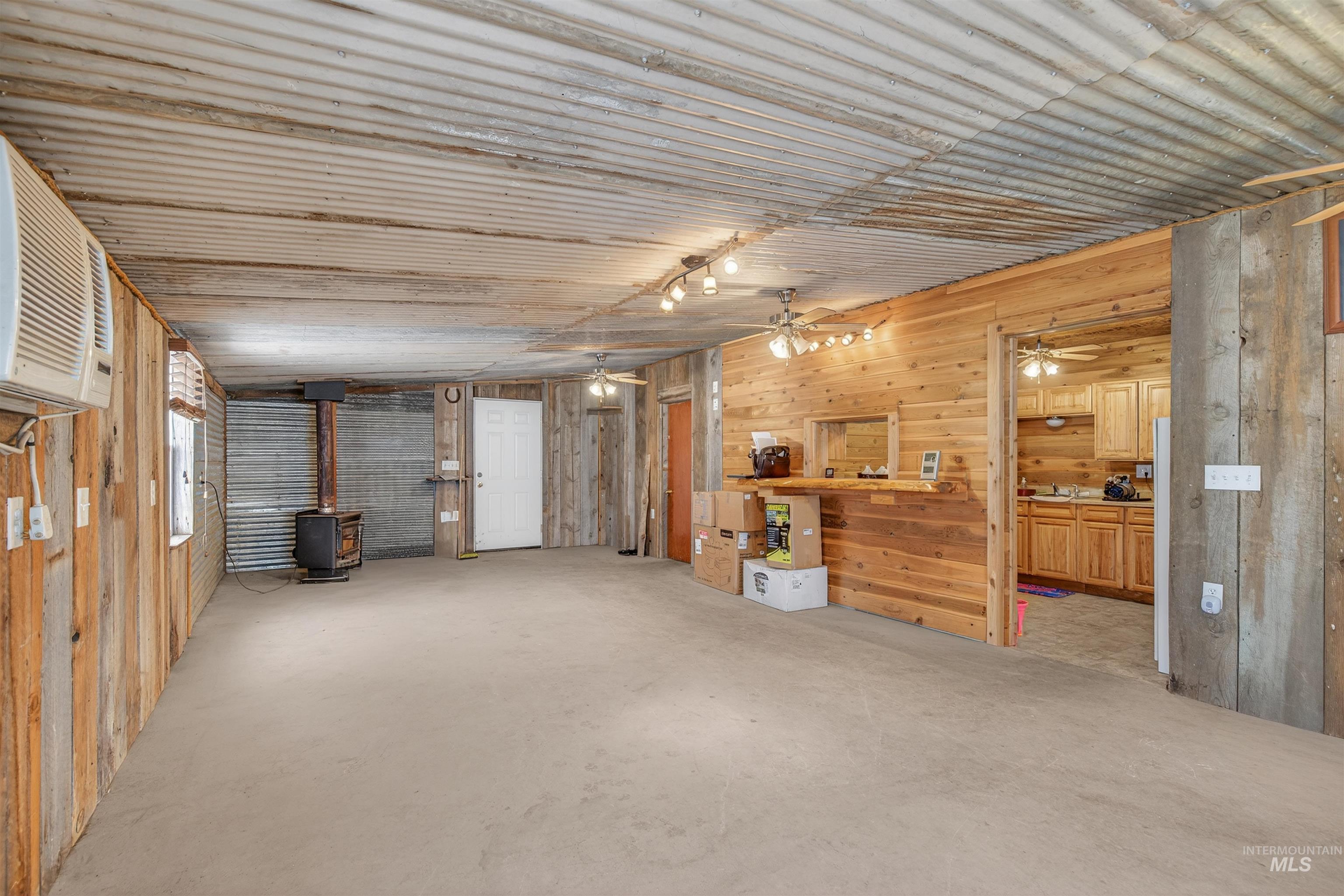 1585 Woodside Road Winchester, ID 83555 - Photo 39 of 47 Living area with a wood stove, wood walls, unfinished concrete flooring, and a ceiling fan