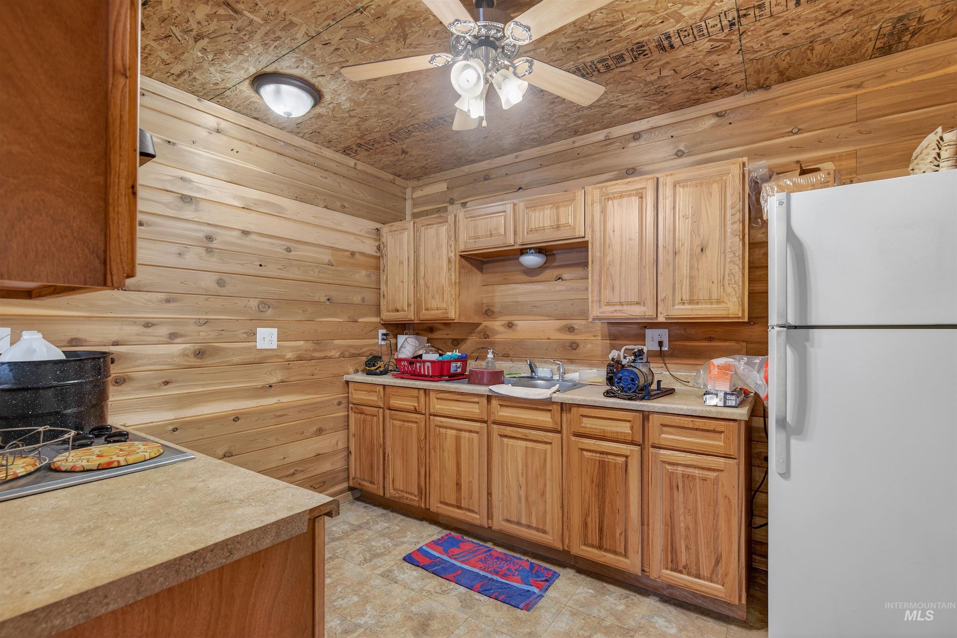 1585 Woodside Road Winchester, ID 83555 - Photo 40 of 47 Kitchen with freestanding refrigerator, light countertops, wood walls, a ceiling fan, and brown cabinets