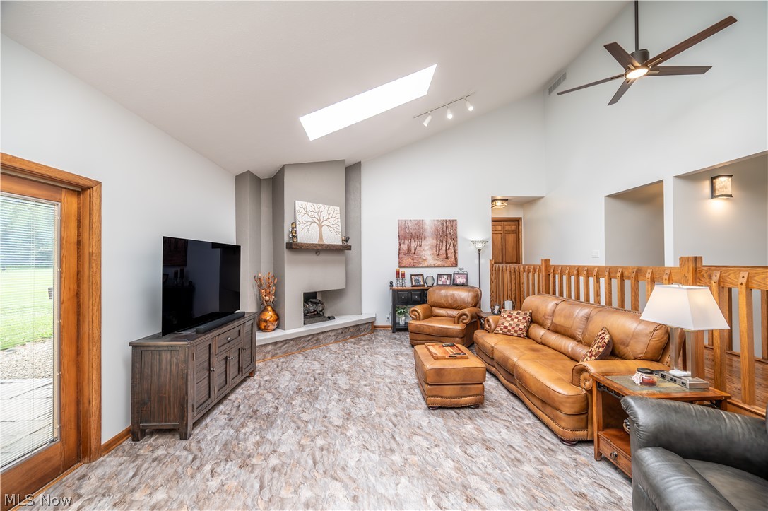 405 Airport Road Northwest Warren, OH 44481 - Photo 7 of 50 Vaulted ceiling living space featuring a central fireplace with stone hearth, wood-finish flooring, a skylight, a ceiling fan, and a wood-framed glass pane door