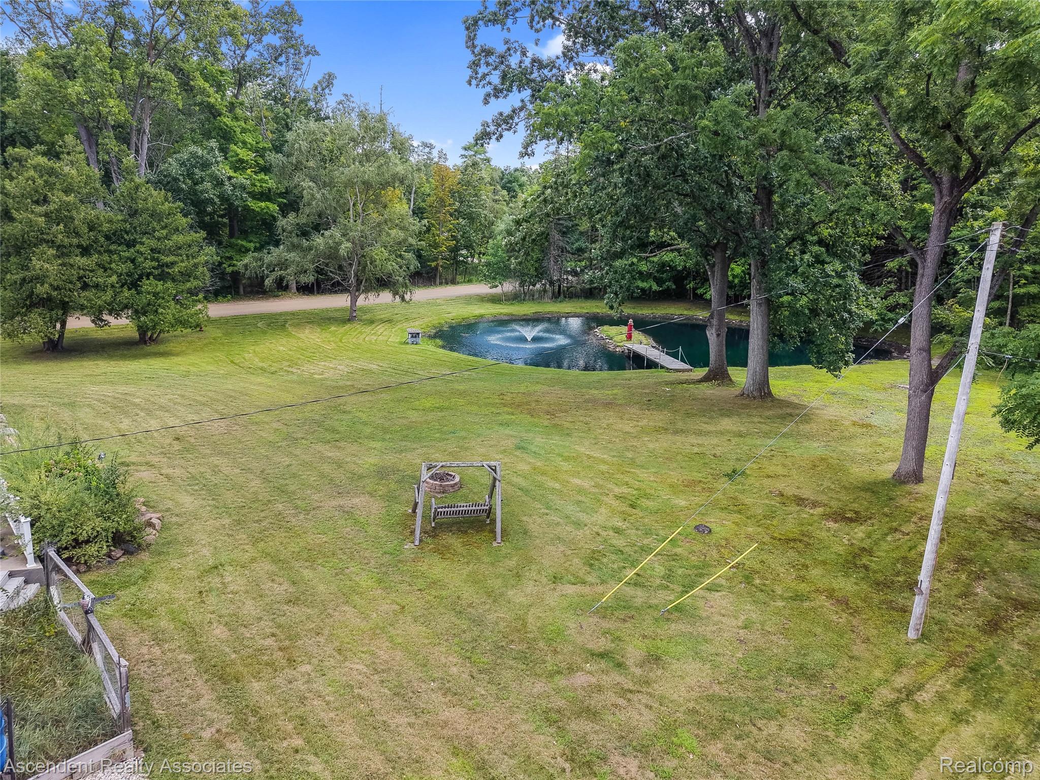 6157 Blue Beech Court Rochester, MI 48306 - Photo 27 of 30 Manicured lawn with a water feature, surrounding mature trees, a wooden dock, and a fire pit