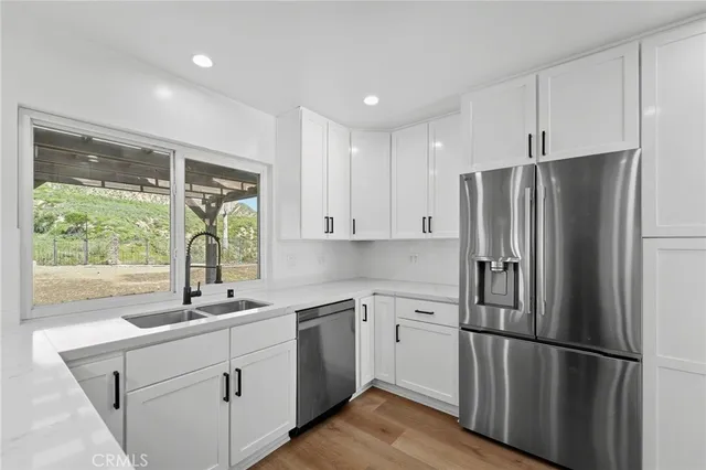 a kitchen with stainless steel appliances granite countertop a stove a sink dishwasher a refrigerator and white cabinets with wooden floor