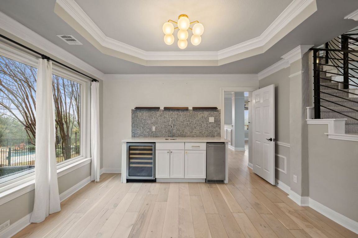 2137 Rivina Drive Austin, TX 78733 - Photo 13 of 39 Bar with white cabinetry, beverage cooler, stairs, decorative backsplash, and crown molding