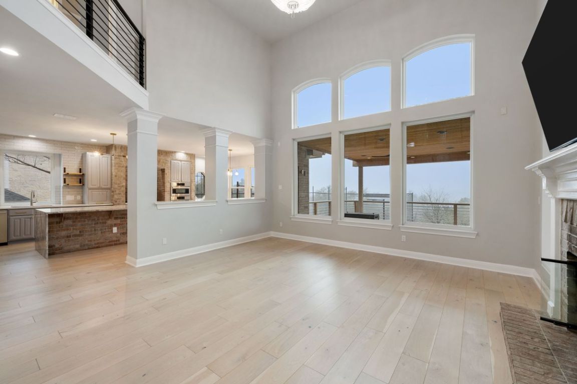 2137 Rivina Drive Austin, TX 78733 - Photo 20 of 39 Unfurnished living room featuring a towering ceiling, light wood-style floors, and a brick fireplace