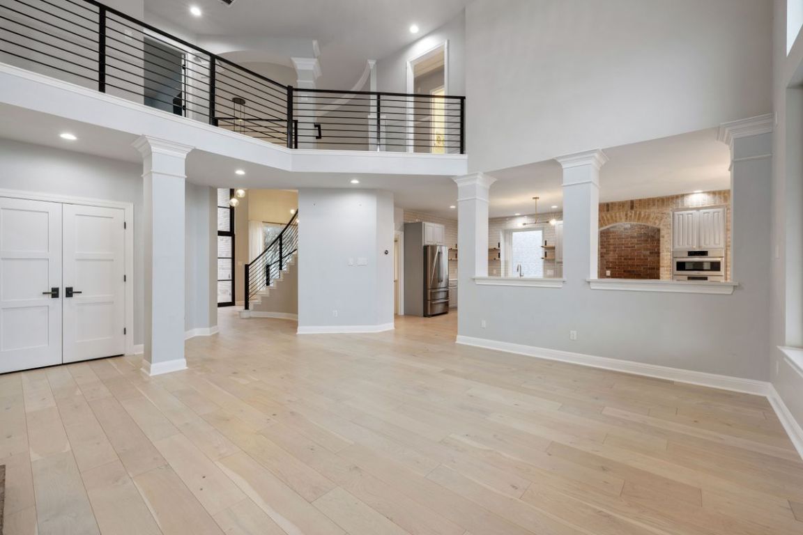2137 Rivina Drive Austin, TX 78733 - Photo 22 of 39 Unfurnished living room featuring a towering ceiling, decorative columns, recessed lighting, light wood finished floors, and stairs