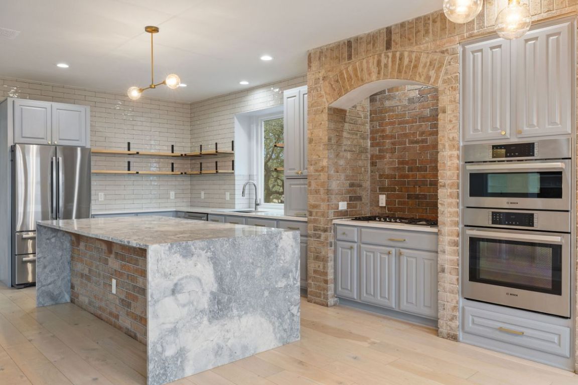 2137 Rivina Drive Austin, TX 78733 - Photo 5 of 39 Kitchen with stainless steel appliances, a kitchen island, gray cabinets, decorative light fixtures, and light stone counters