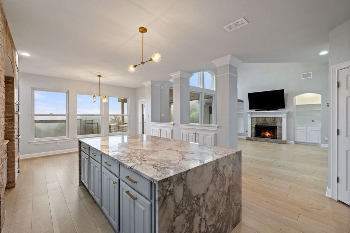2137 Rivina Drive Austin, TX 78733 - Photo 6 of 39 Kitchen with gray cabinets, a fireplace, light wood finished floors, pendant lighting, and a center island
