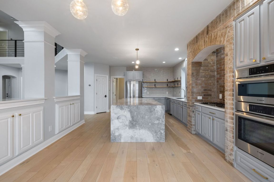 2137 Rivina Drive Austin, TX 78733 - Photo 7 of 39 Kitchen featuring gray cabinets, open shelves, stainless steel appliances, decorative light fixtures, and backsplash