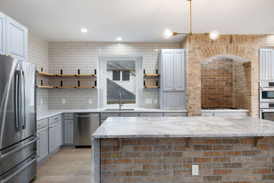 2137 Rivina Drive Austin, TX 78733 - Photo 8 of 39 Kitchen with light stone counters, stainless steel appliances, gray cabinets, a center island, and open shelves
