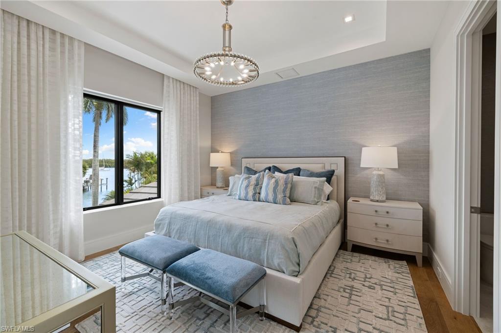 2345 Tarpon Road Naples, FL 34102 - Photo 32 of 43 Bedroom featuring wallpapered walls, an accent wall, hanging lights, light wood-type flooring, and a water view