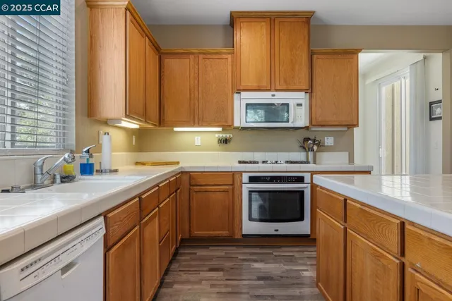 a kitchen with stainless steel appliances granite countertop a refrigerator a sink dishwasher a oven and a dining table with wooden floor