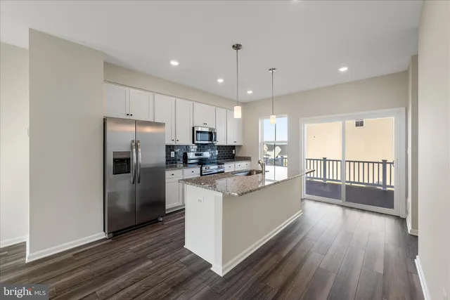 a kitchen with stainless steel appliances granite countertop a refrigerator a sink dishwasher a stove and white countertops with wooden floor