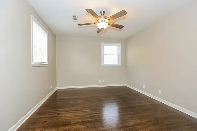 an empty room with wooden floor fan and windows