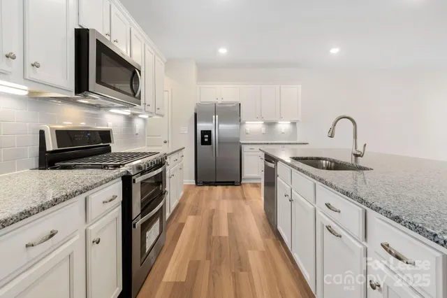 a kitchen with stainless steel appliances granite countertop a sink a stove top oven a refrigerator with wooden cabinets and floor