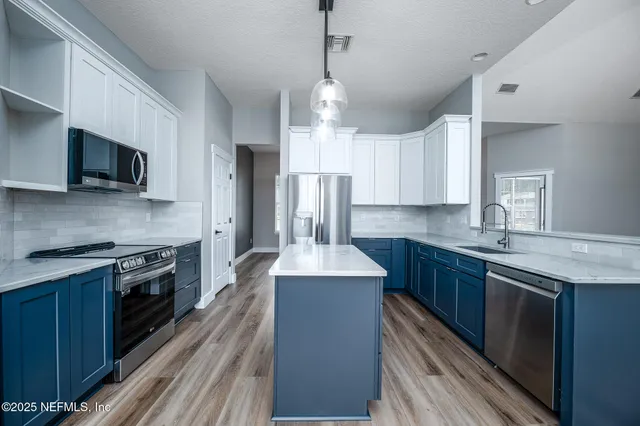 a kitchen with stainless steel appliances granite countertop a refrigerator a sink dishwasher a stove and white countertops with wooden floor