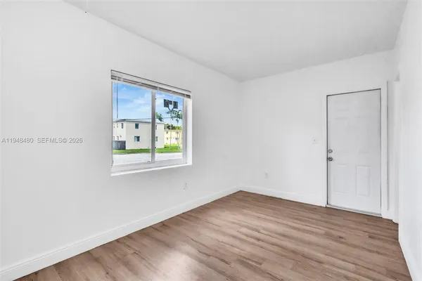 a view of an empty room with wooden floor and a window