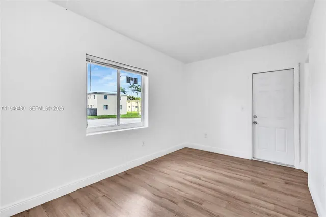 a view of an empty room with wooden floor and a window