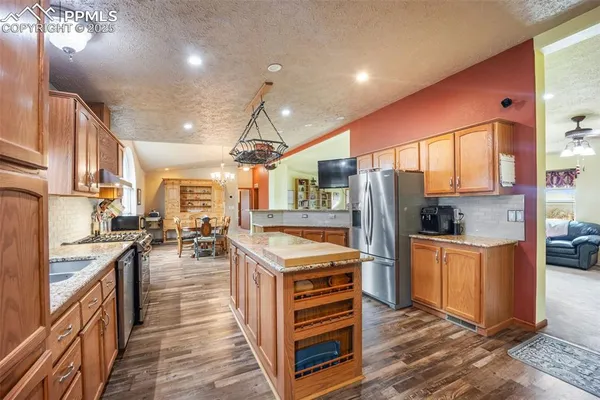 a kitchen with stainless steel appliances kitchen island granite countertop a refrigerator oven a sink dishwasher and wooden cabinets with wooden floor