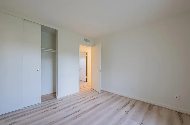 a view of an empty room with wooden floor and closet