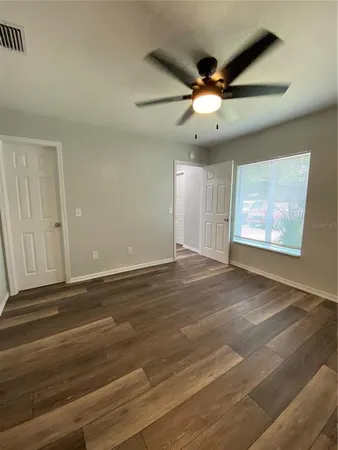 an empty room with wooden floor ceiling fan and windows