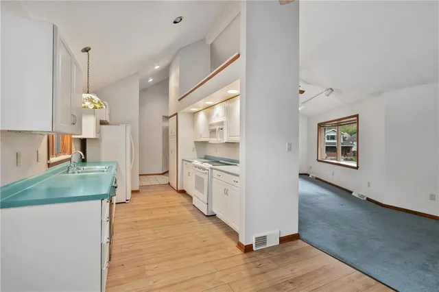 a large white kitchen with a refrigerator a stove a sink and a wooden floor