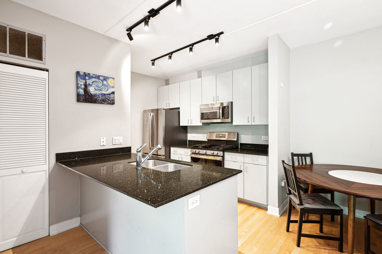 4311 North Sheridan Road, Unit 303 Chicago, IL 60613 - Photo 5 of 17 a kitchen with stainless steel appliances granite countertop a sink a stove a microwave a dining table and chairs with wooden floor