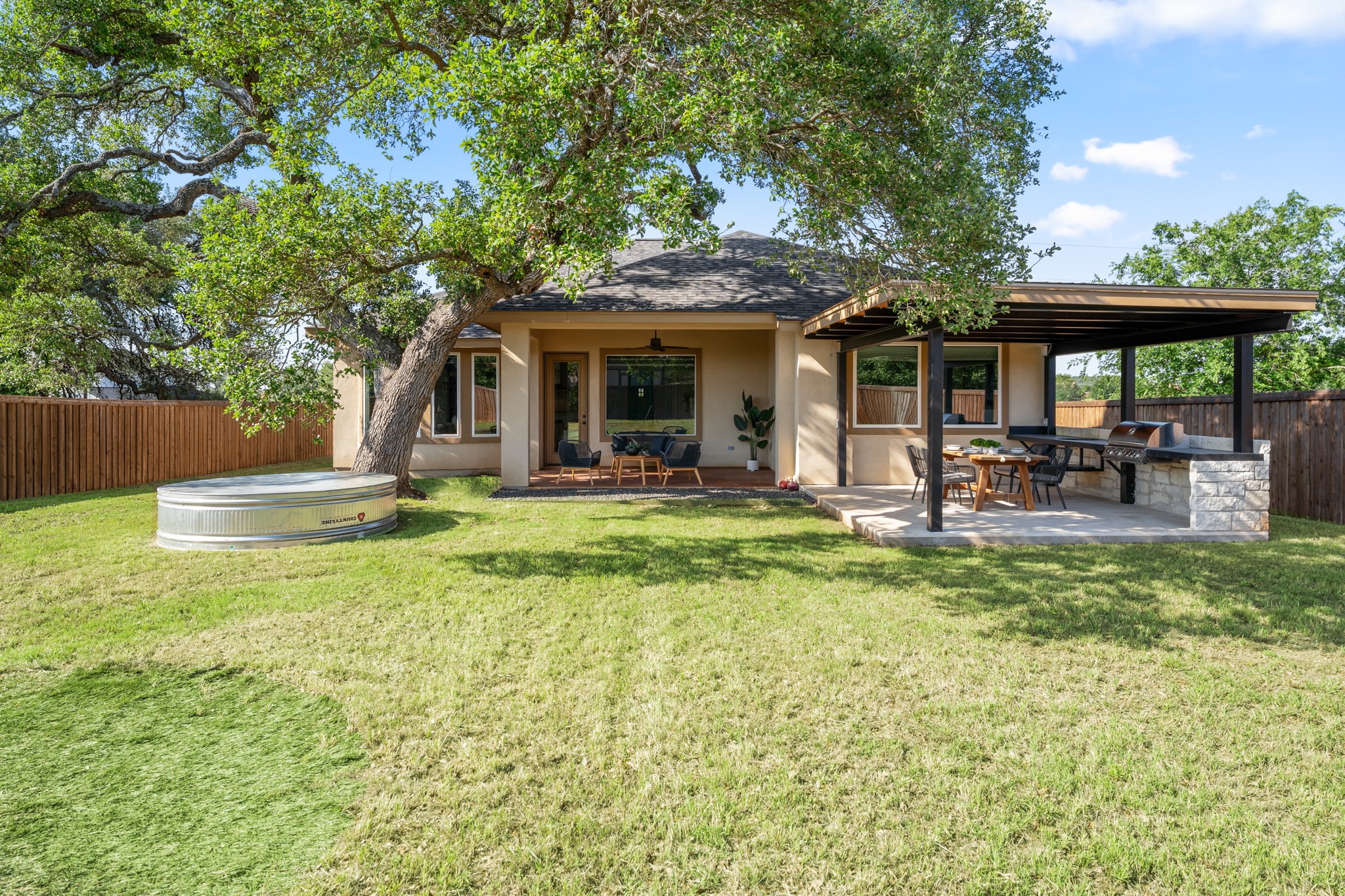 128 Hiram Cook Blanco, TX 78606 - Photo 30 of 40 Spacious backyard featuring a built-in outdoor kitchen with stone accents, an attached covered patio, and a large mature tree providing natural shade