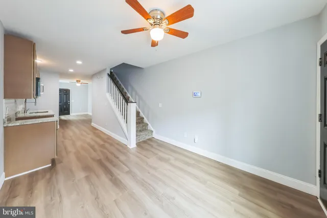 a view of an empty room with wooden floor and a ceiling fan